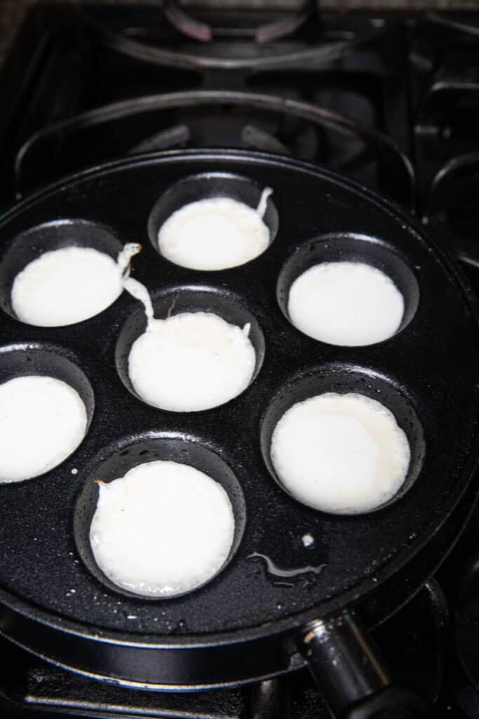 Coconut mixture inside kanom krok slotted round shaped pan on a stove.