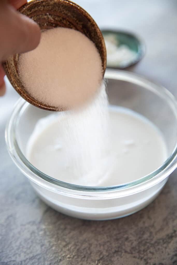 A cup pouring sugar into coconut mixture for thai coconut pancakes.