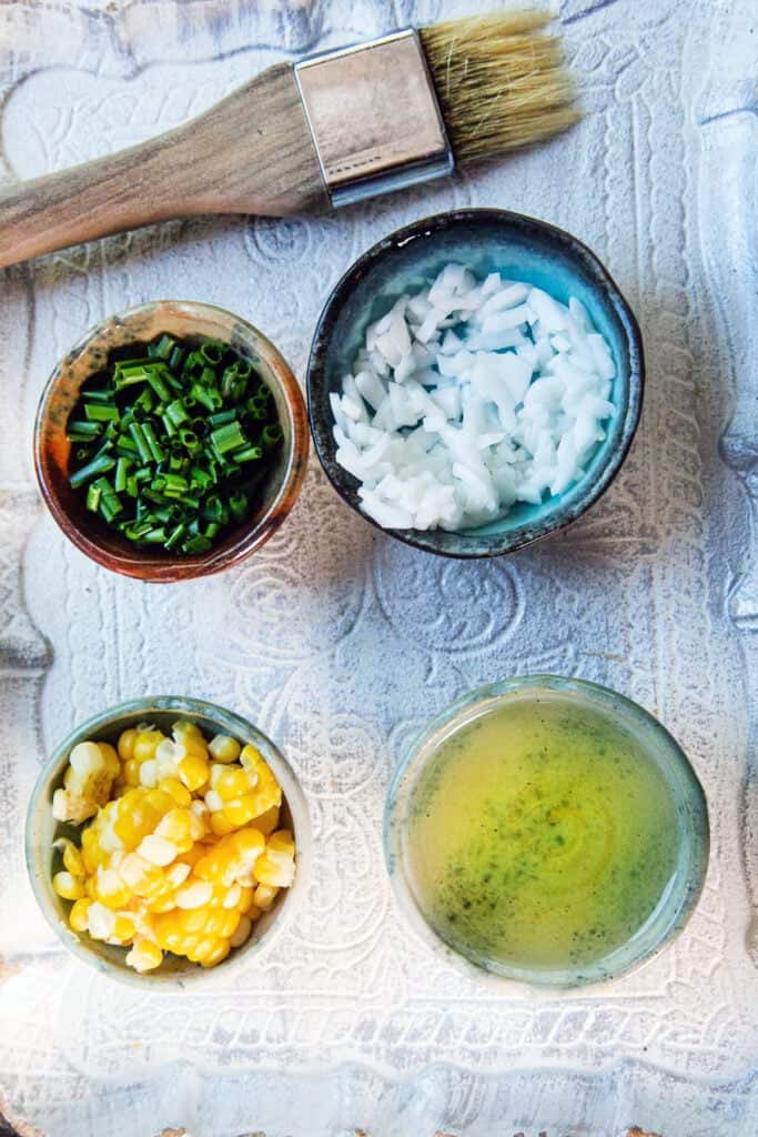 Chopped chives, coconut flesh, corn kernels and oil on a tray for kanom krok toppings.