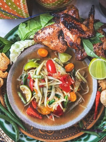 A plate of som tum or Thai papaya salad with grilled chicken on the side.