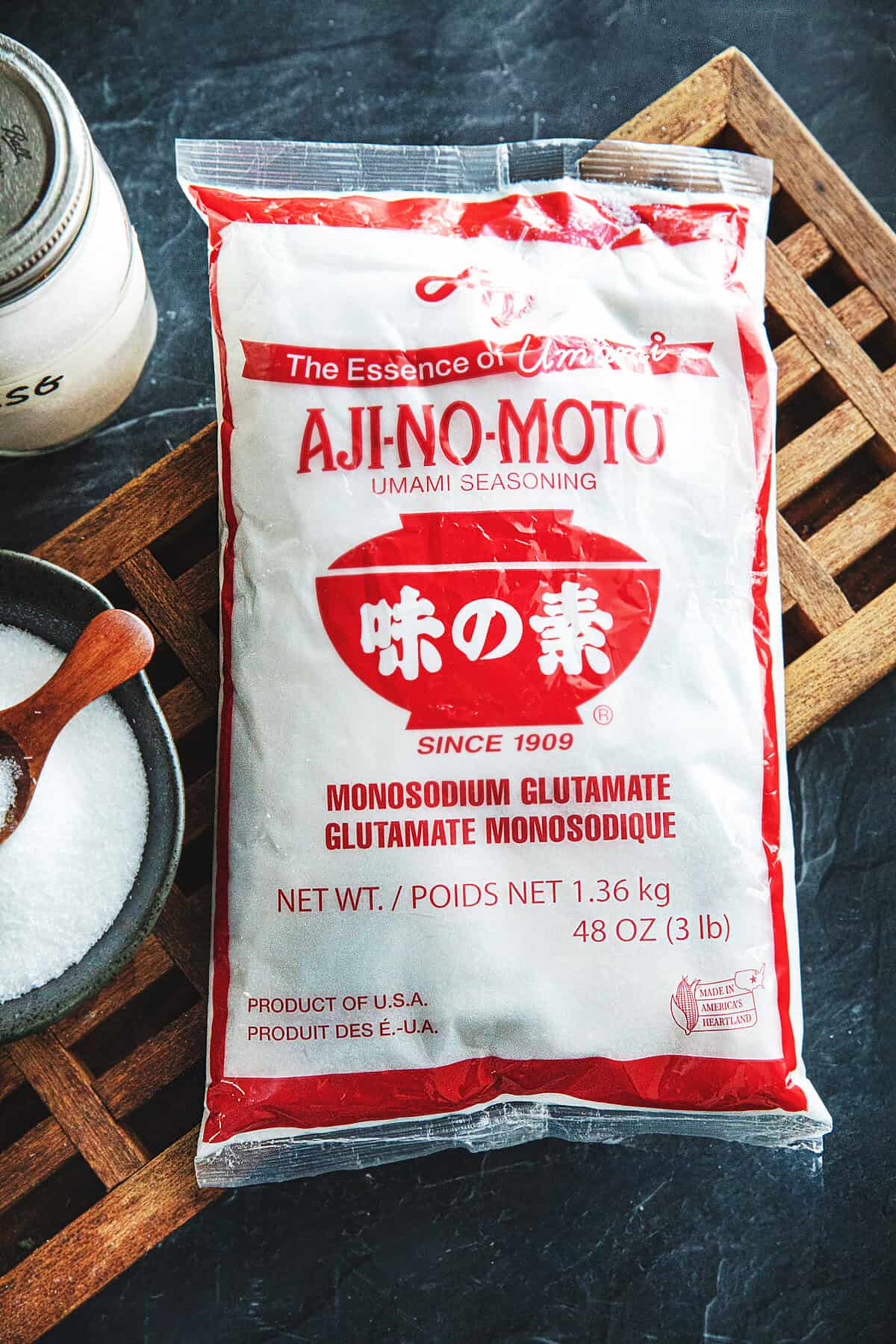 A bag of MSG labeled Ajinomoto on a cutting board on a table.
