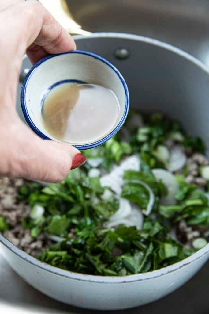 Fingers holding Pla Ra in a bowl over laab moo salad.