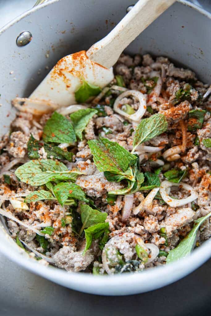 laab moo salad mixture in a pot with mint leaves and spatula in side.