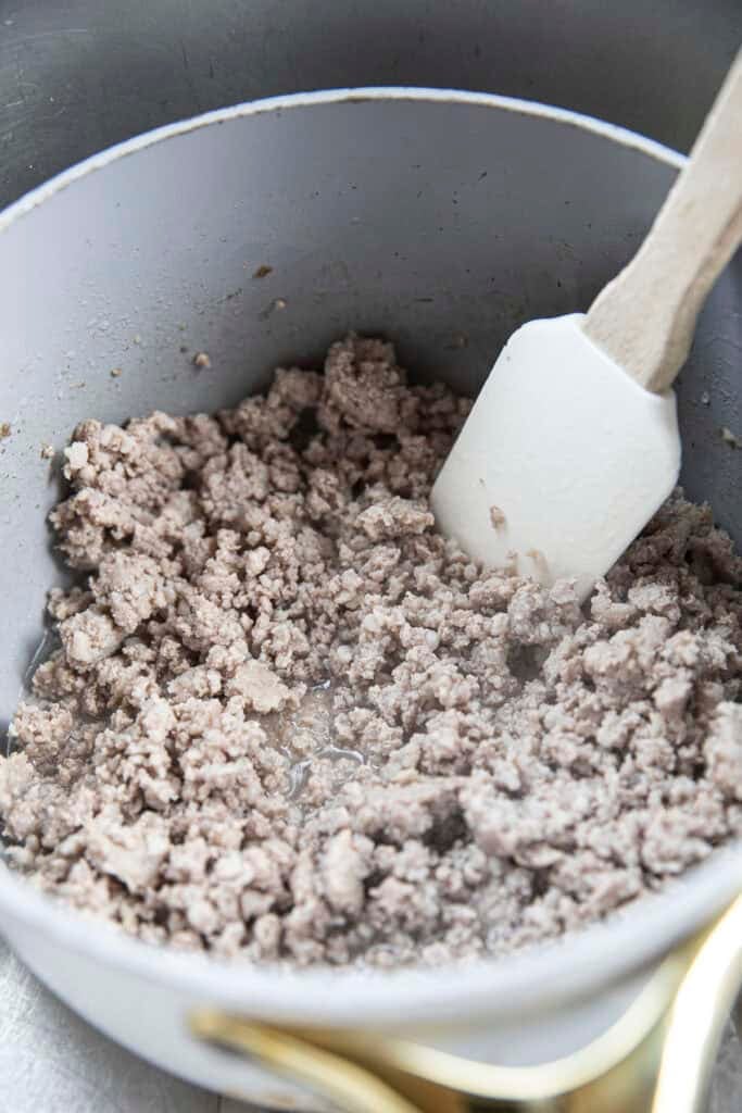 Cooked ground pork in a pot with water and a spatula inside.