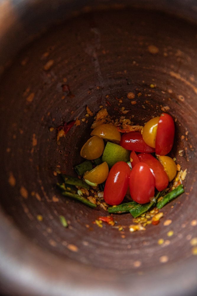 lightly crushed Tomatoes and green beans in a mortar.