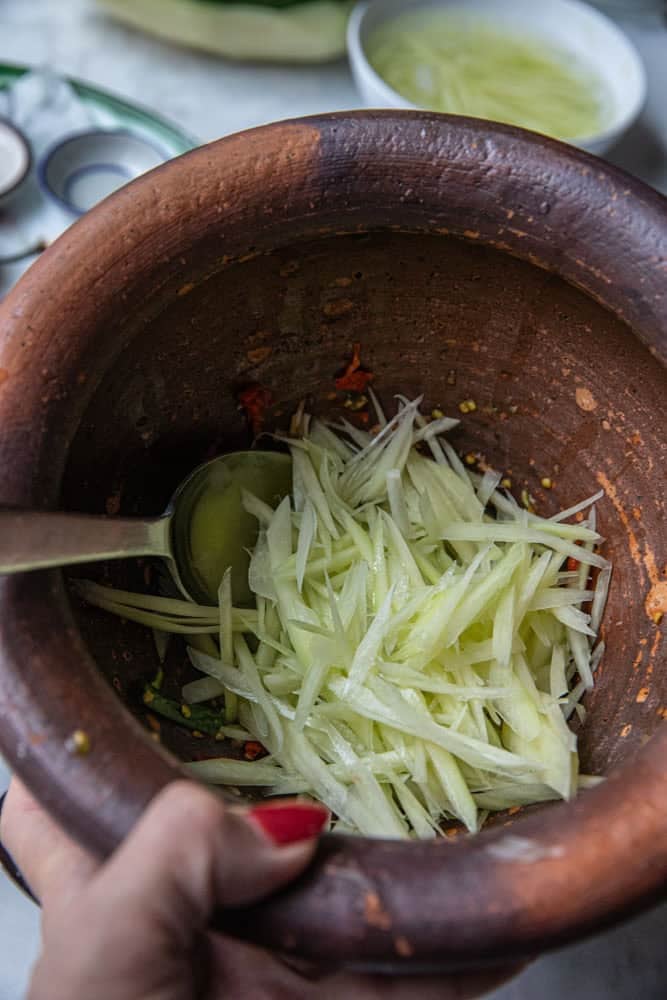 Shredded green papaya in a mortar on the table.