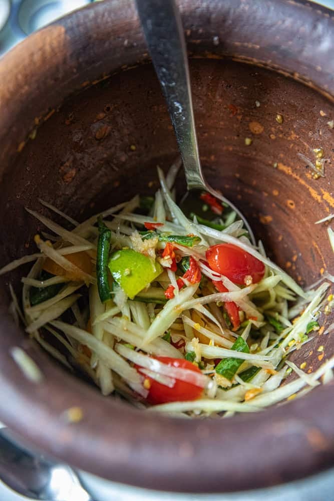 A spoon scooping papaya salad in mortar.