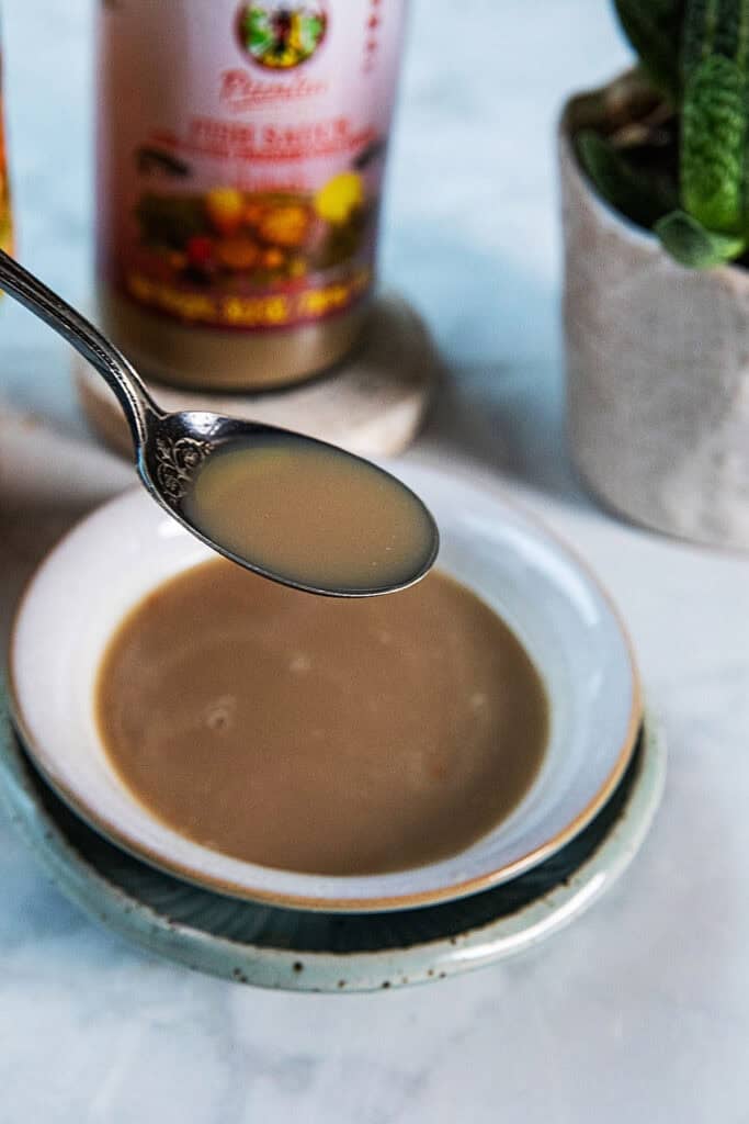 A spoon with Pla Ra sauce over a bowl on the table.