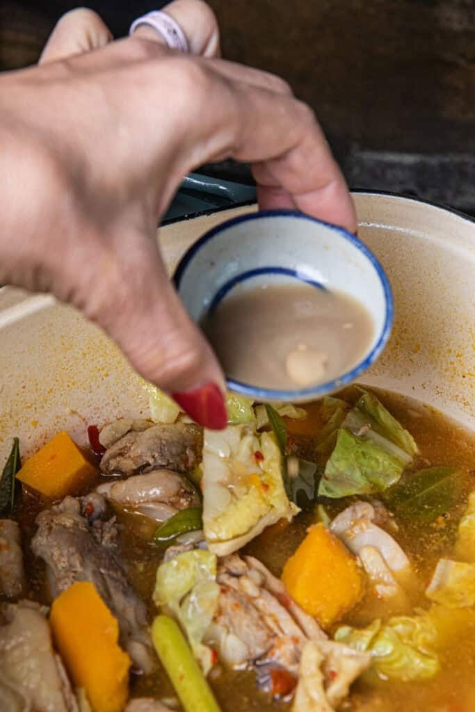 Adding pla ra fermented fish sauce to Gaeng Om Gai for authentic Isaan flavor