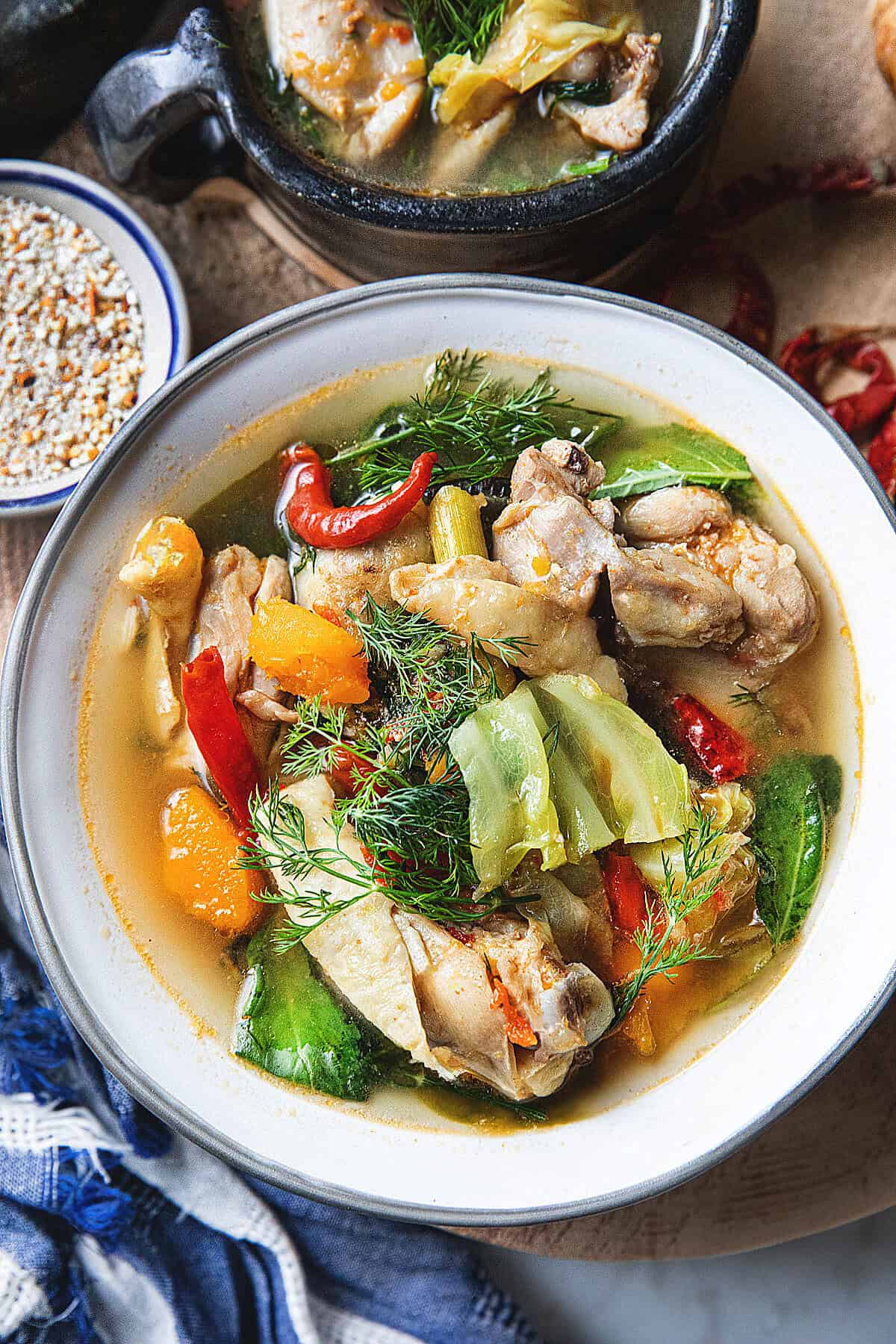 Close up of Gaeng Om Gai Thai chicken soup with squash, cabbage, herbs, and chilies in a light broth. 