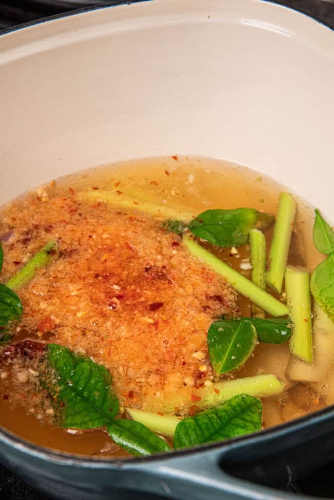 Lemongrass, galangal, and makrut lime leaves and chili paste simmering in water for Gaeng Om Gai broth