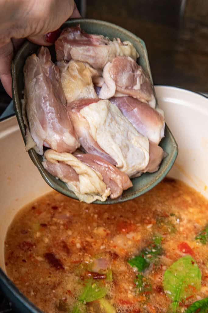 Adding raw chicken pieces to Gaeng Om Gai broth before simmering.