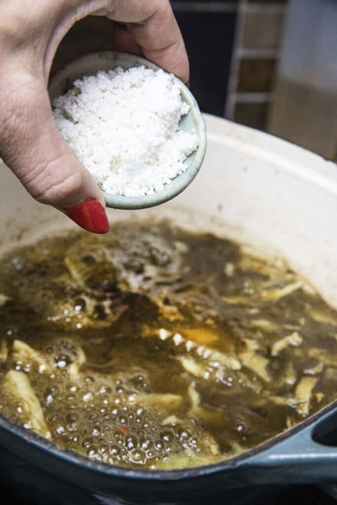 Sticky rice paste in a bowl pouring in to a pot of gaeng nor mai soup.