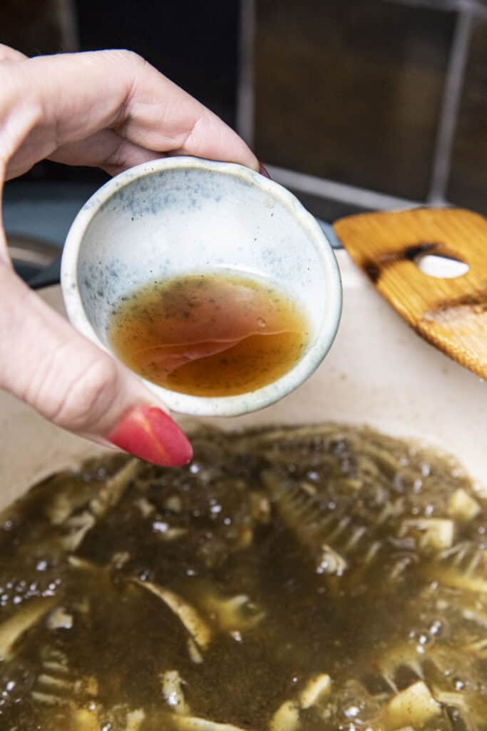 Fish sauce in a bowl pouring in to a pot of gaeng nor mai soup.