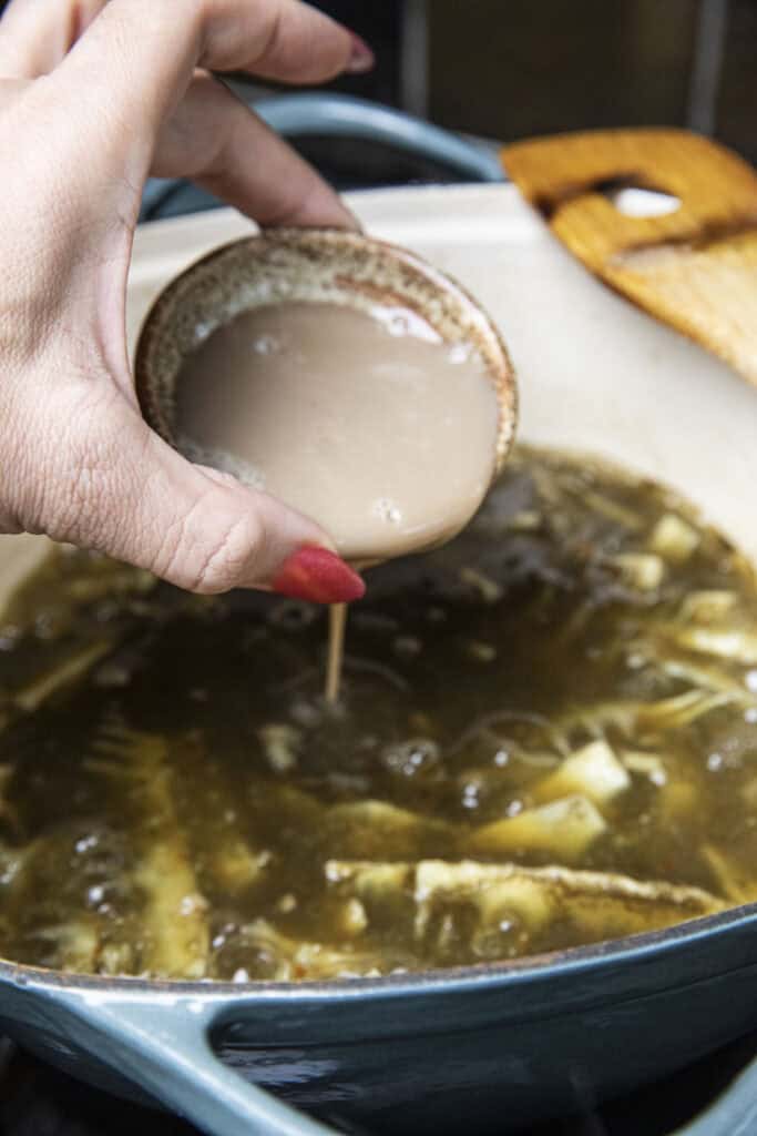 Pla Ra fermented Fish sauce in a bowl pouring in to a pot of gaeng nor mai soup.