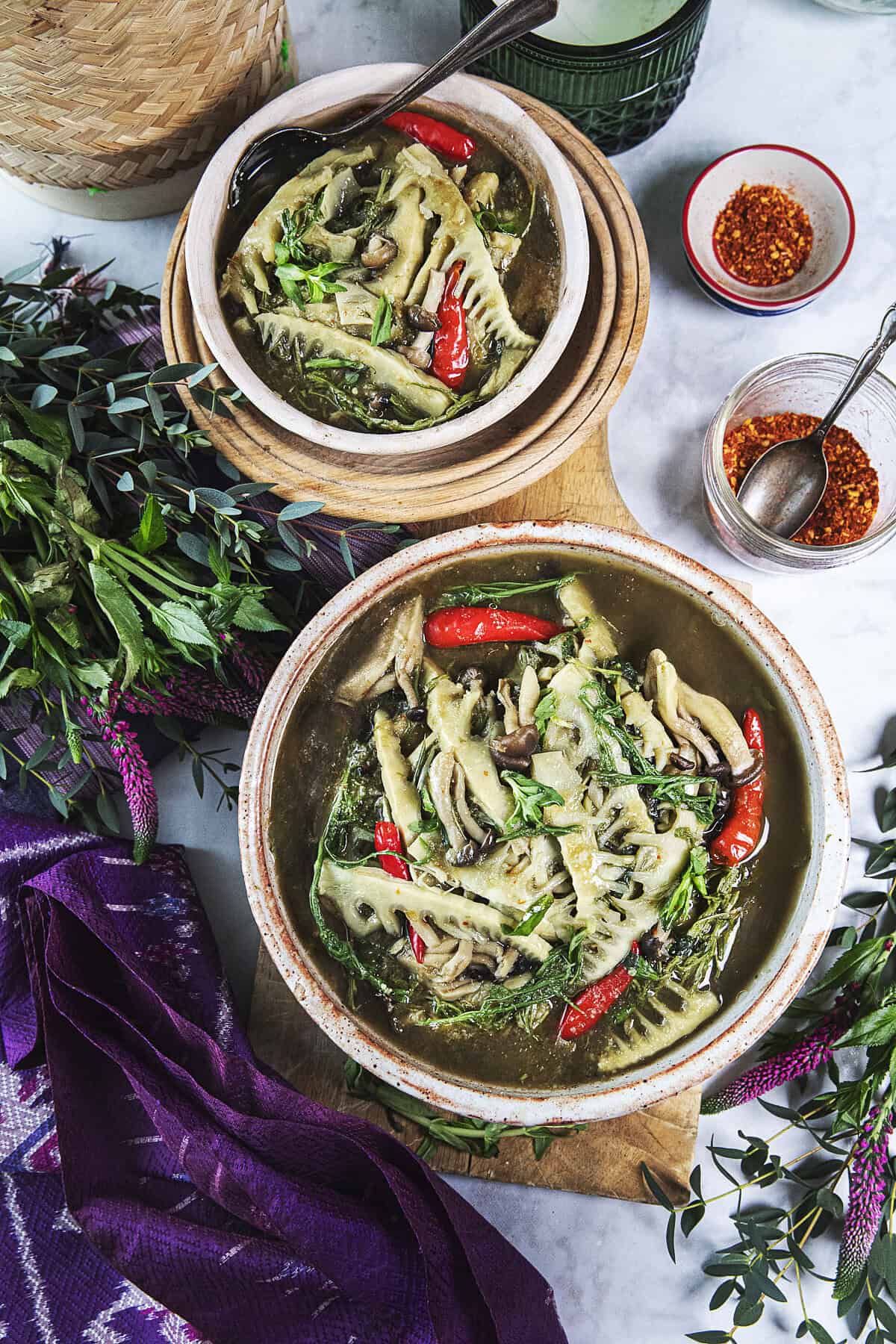 Isaan bamboo shoot soup in bowls on the table with chili flakes and sticky rice basket.