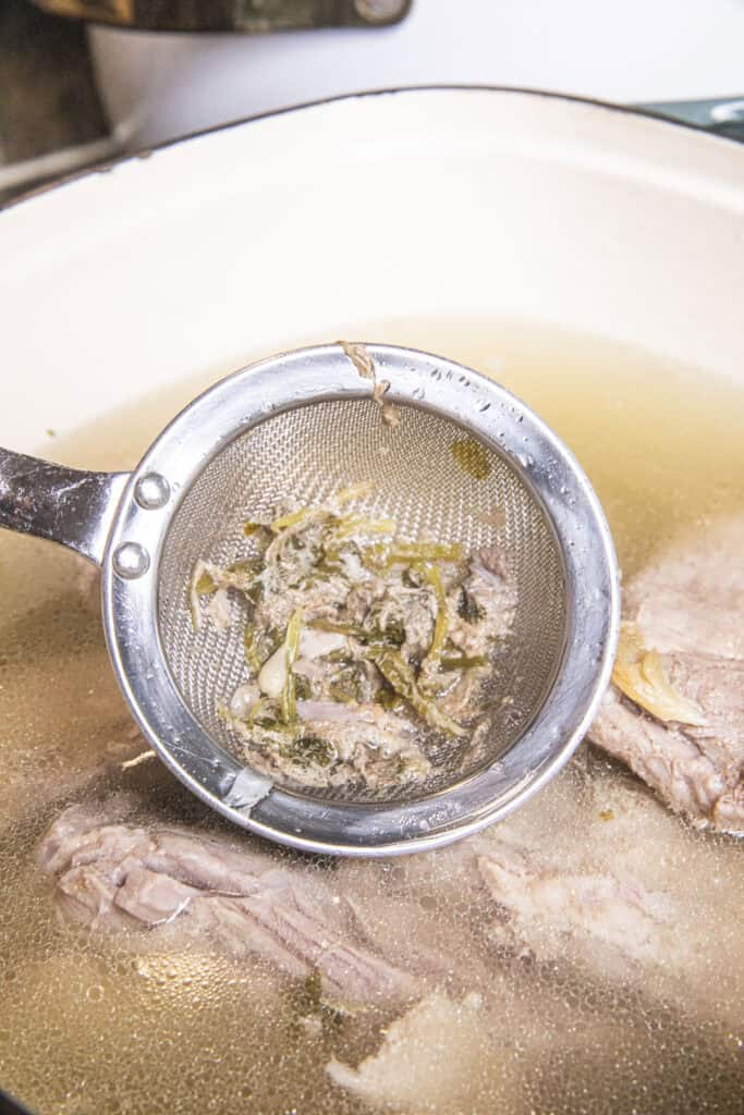 A metal strainer skimming impurities from a pot.