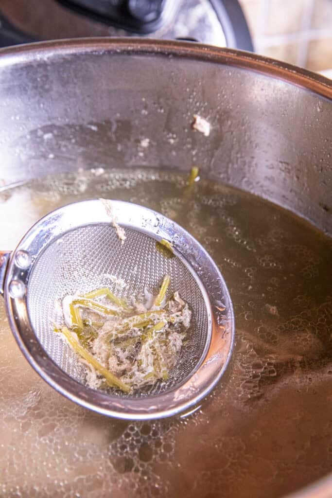 Metal Strainer skimming Leng Saeb broth from a pot.