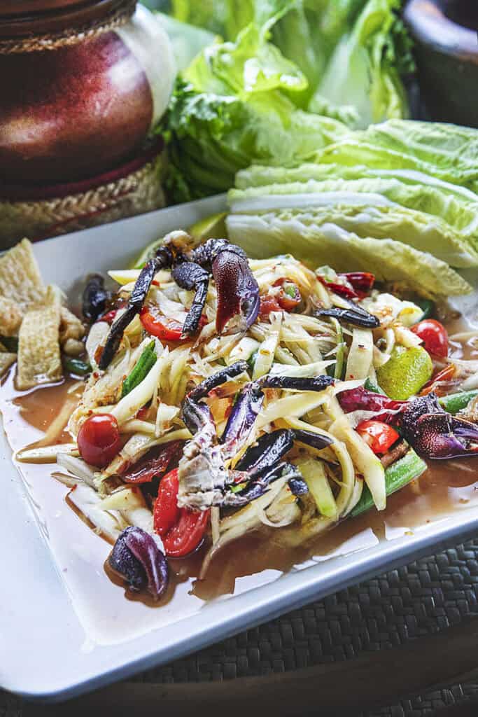 Isaan Pu Pla Ra papaya salad on plate with rice and vegetables on the side.