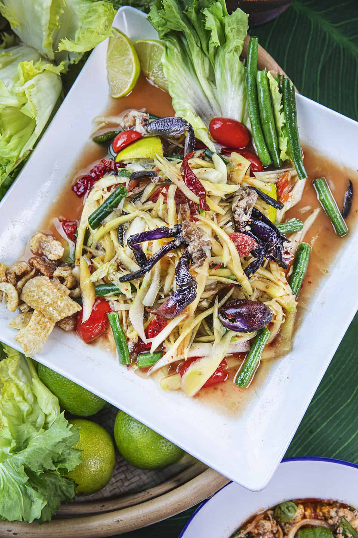 Som tum pu pla ra salad on a plate with veggie around. 