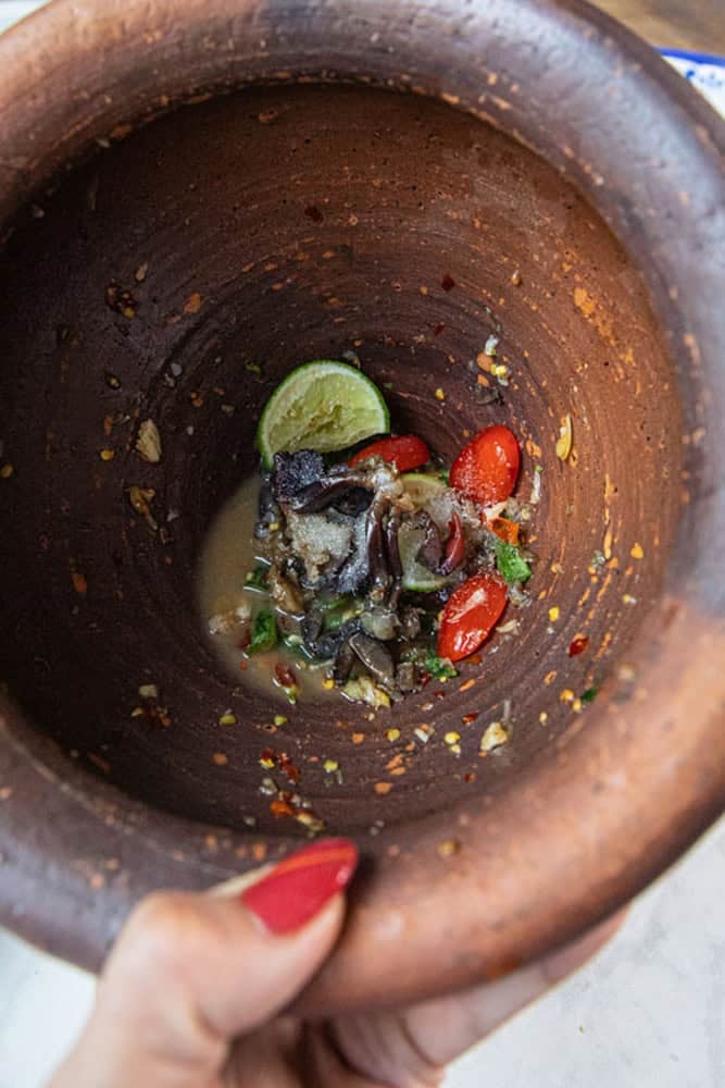 Fermented crab added to papaya salad in a clay mortar.