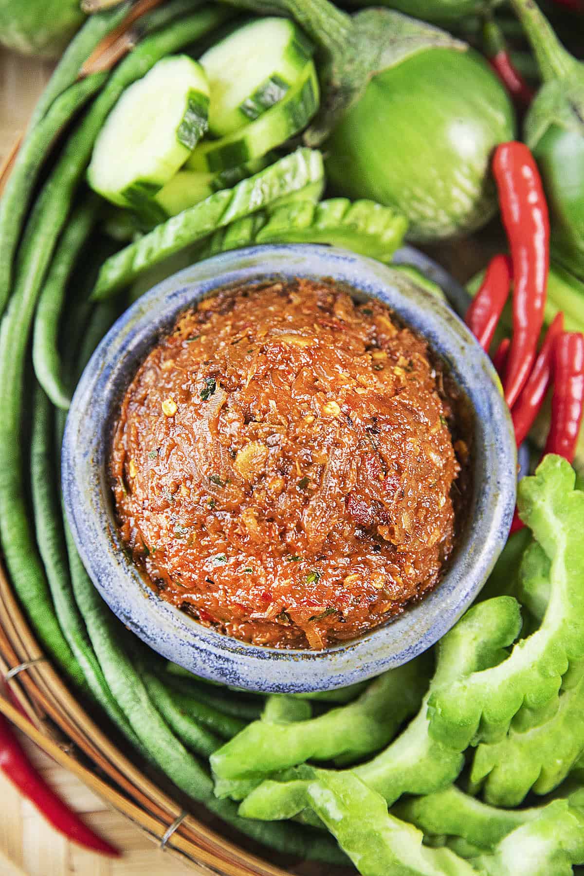 Jeow Bong paste in a bowl surrounded by veggies in an Isaan home-style kitchen setting.