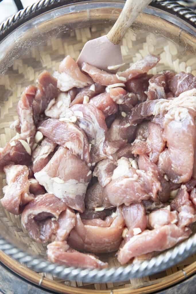 Adding chopped garlic to marinated pork for Moo Tod.