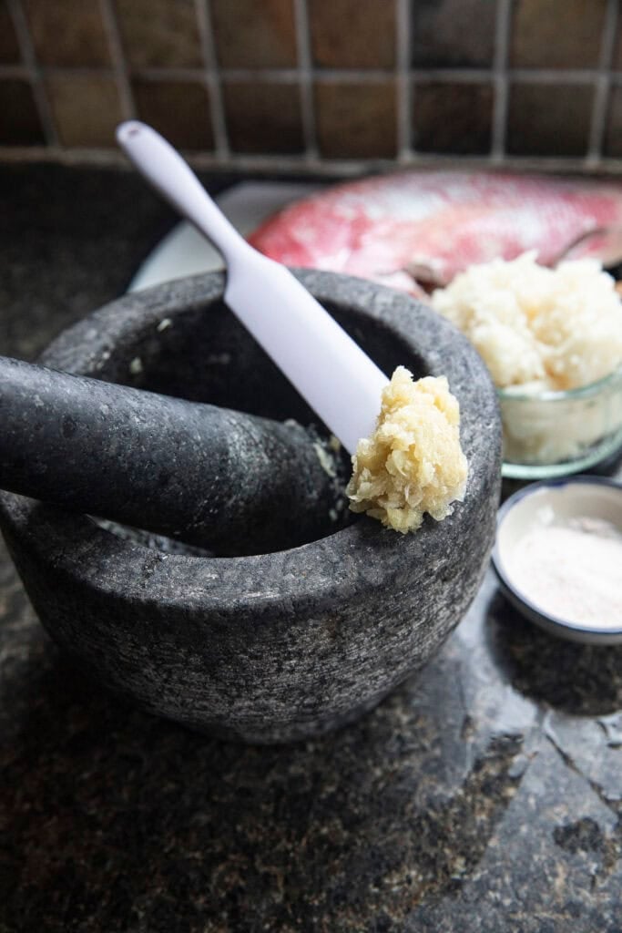 Garlic being pounded in a mortar for Thai Pla Som fermentation.