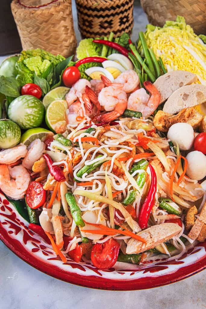 Close up of Som Tum Mua loaded Thai papaya salad with noodles, long beans, tomatoes, and dried shrimp.