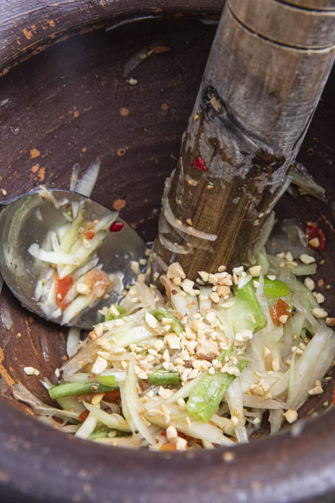 mixing thai papaya salad and peanuts in clay mortar.
