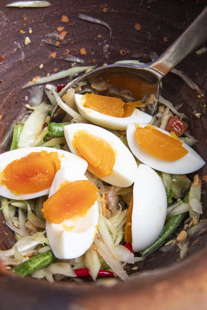 mixing salted duck eggs to thai papaya salad in clay mortar.