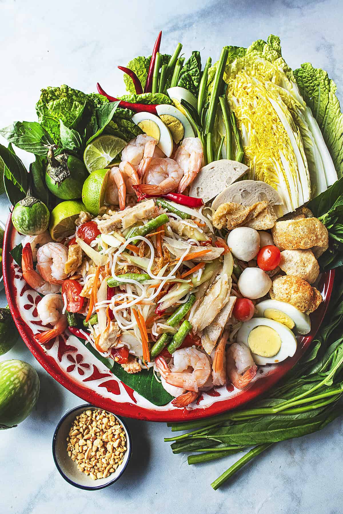 A platter of Som Tum Mua loaded Thai papaya salad with noodles, long beans, tomatoes, and dried shrimp.