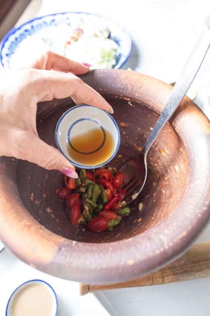 Adding fresh fish sauce to the dressing in a clay mortar for Som Tum Mua papaya salad