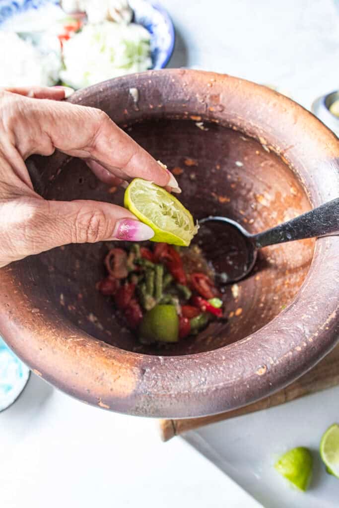 Adding fresh lime juice to the dressing in a clay mortar for Som Tum Mua papaya salad