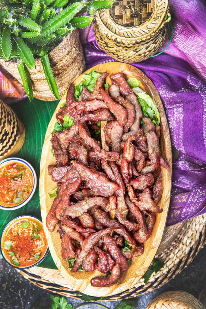 Thai pork jerky on a plate served with sticky rice in bamboo baskets.