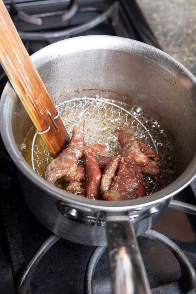 Thai pork jerky moo dad deaw frying in oil in a pot.