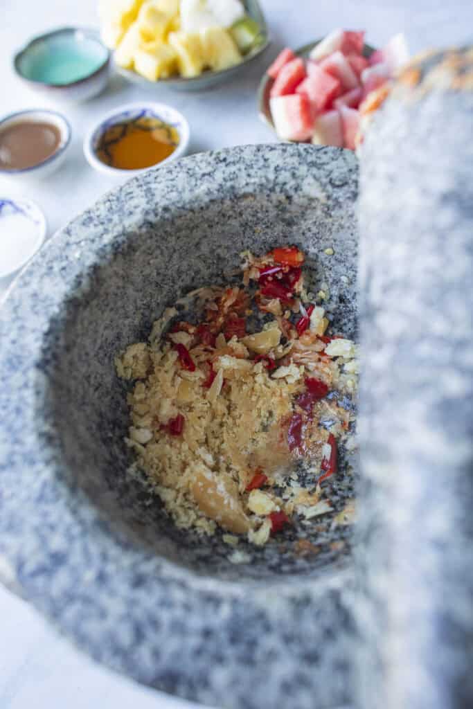 Pounding chilies garlic for som tum dressing in a mortar and pestle.