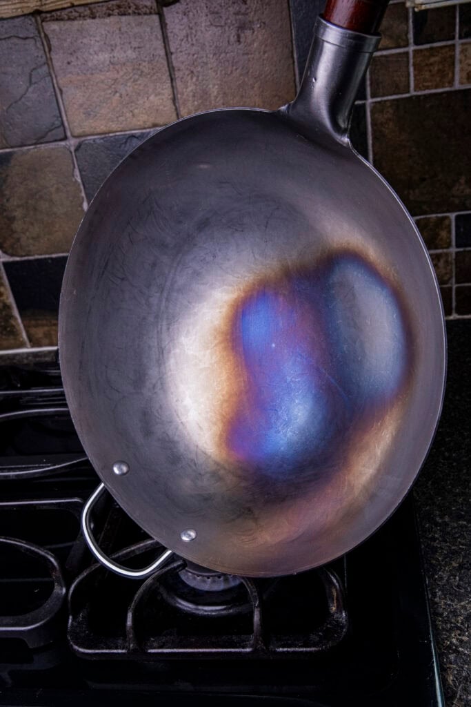 Heating a carbon steel wok over a gas burner before adding oil.