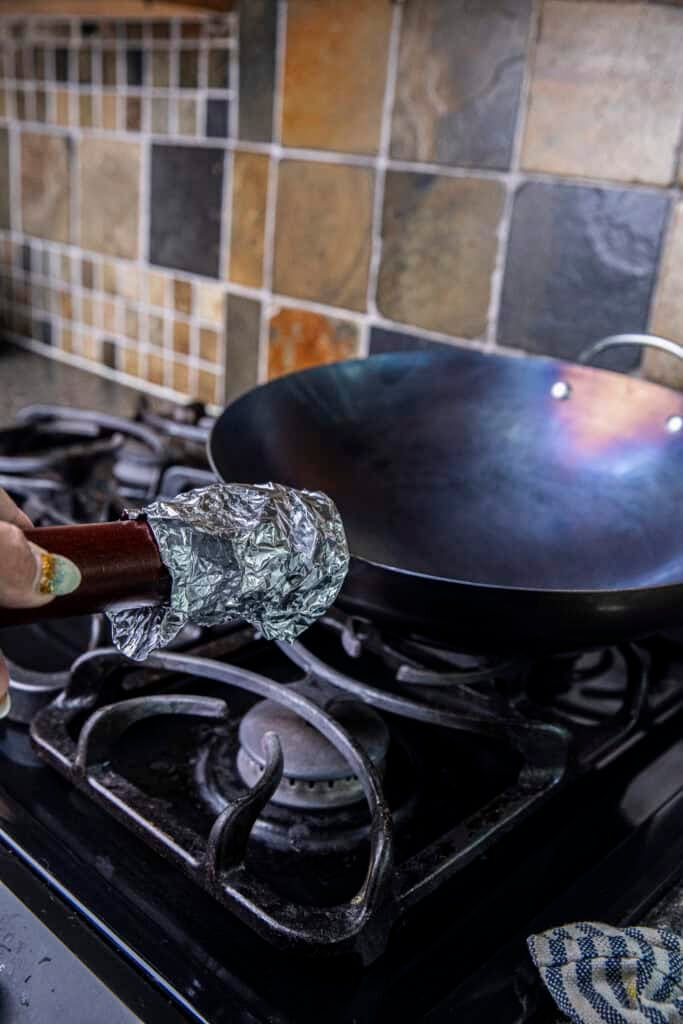 Protecting the wok handle from heat with aluminum foil during seasoning.