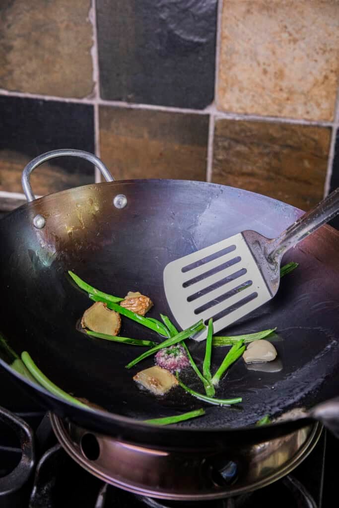 Frying aromatics in a newly seasoned wok to remove factory smell and chemicals.
