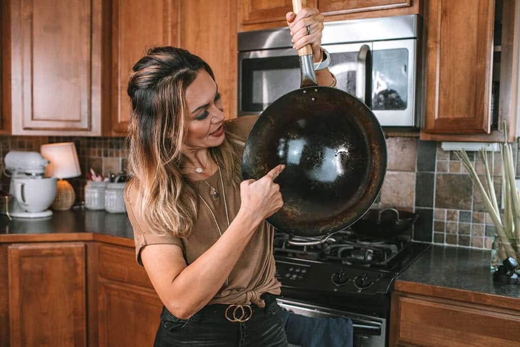 Thai food blogger holding a seasoned carbon steel wok showing the patina in the wok from over the years.