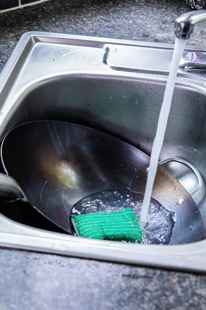 Rinsing a carbon steel wok after seasoning and cleaning.