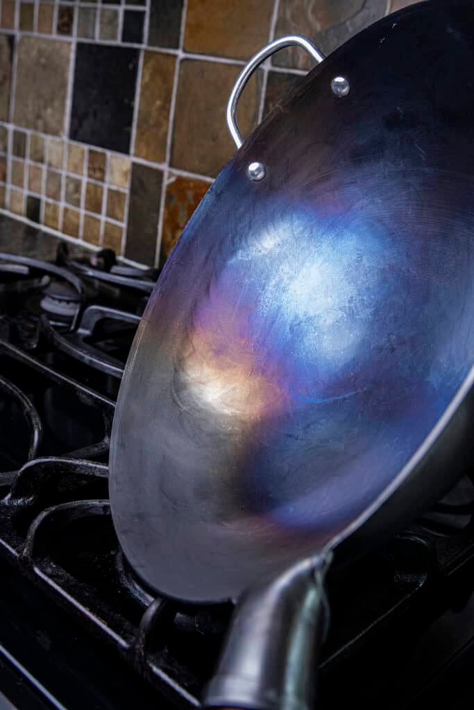 Rotating a carbon steel wok over a gas flame to season the sides evenly.