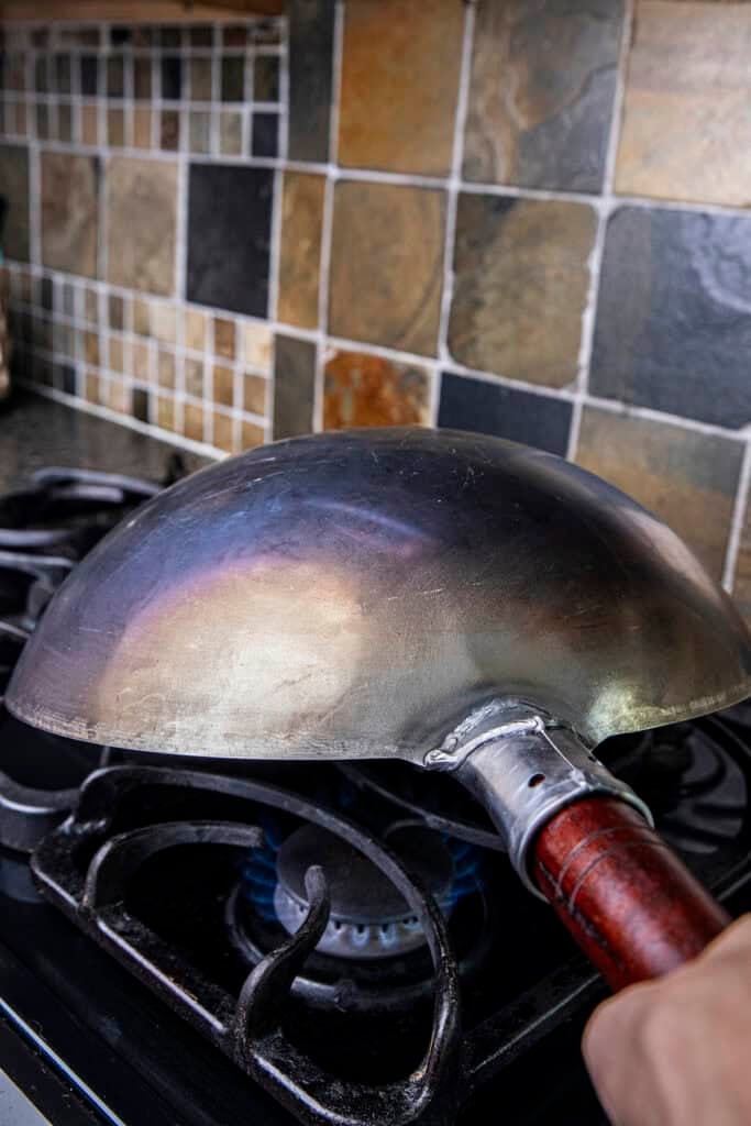 Flipping a carbon steel wok over a gas flame to season the inside evenly.