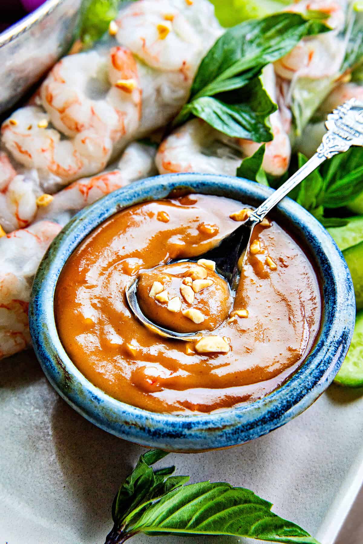 Spicy Hoisin Peanut sauce in a bowl surrounded by shrimp spring rolls.