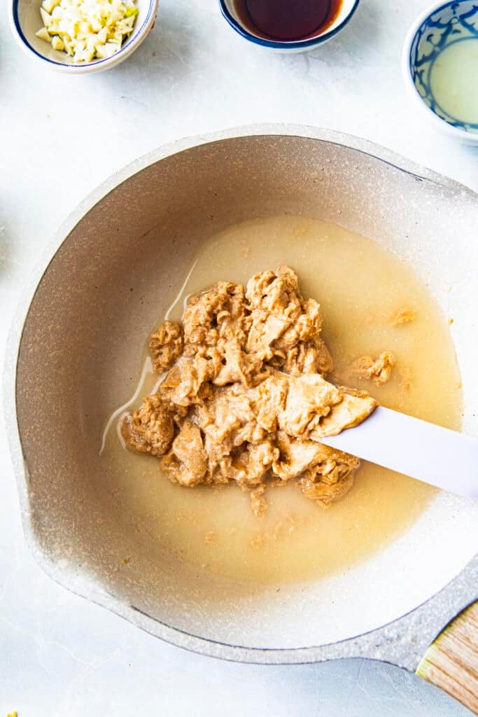 Peanut butter and water for Spicy Hoisin Peanut sauce in a pot with spatula.