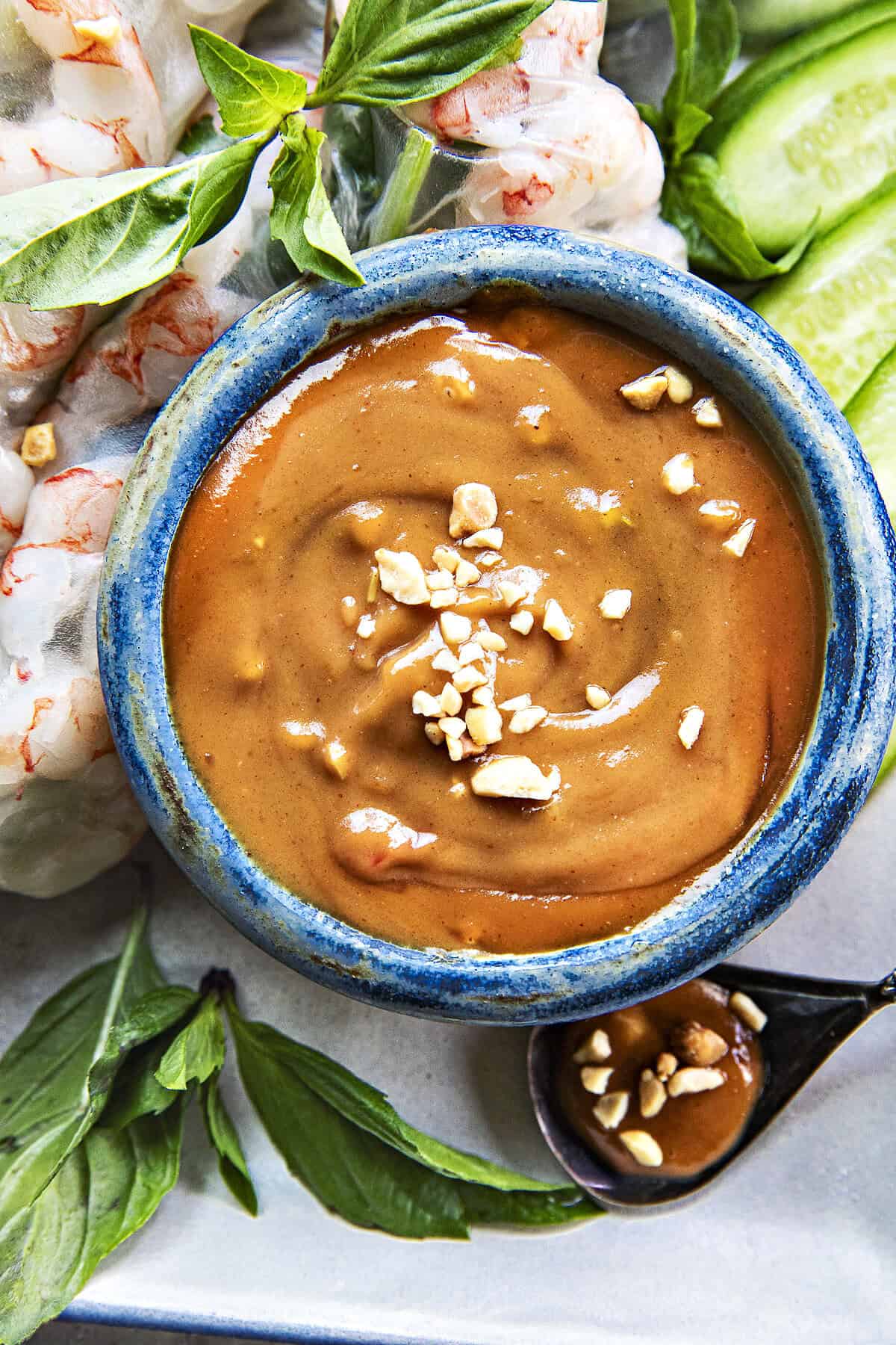 Spicy Hoisin Peanut sauce in a bowl surrounded by shrimp spring rolls.