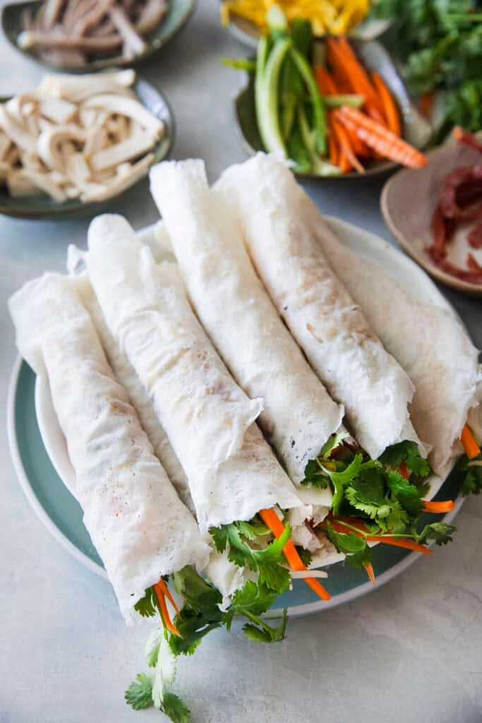 Thai fresh spring rolls, Po Pia Sod, rolled up on a plate with vegetable garnishes on the side.