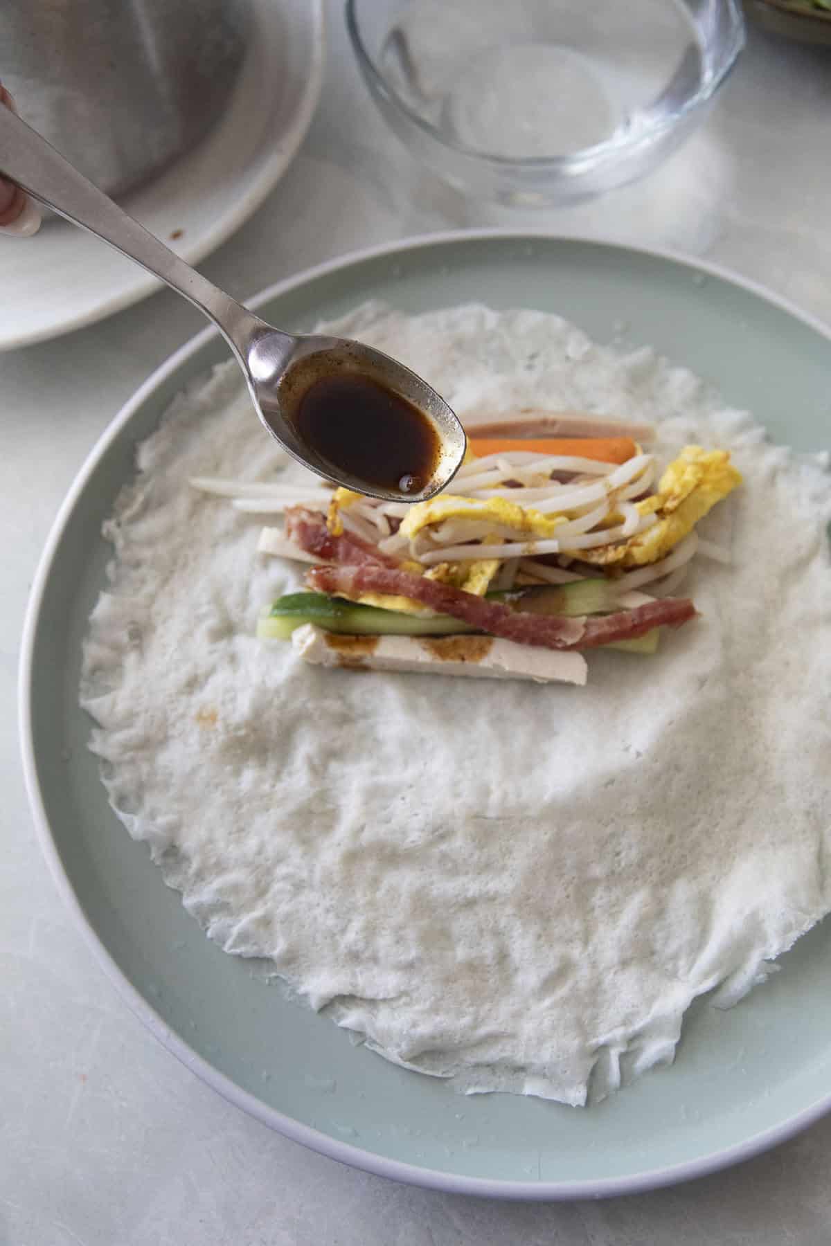 Adding Poh Pia Sod sauce over the filling before rolling a Thai fresh spring roll.