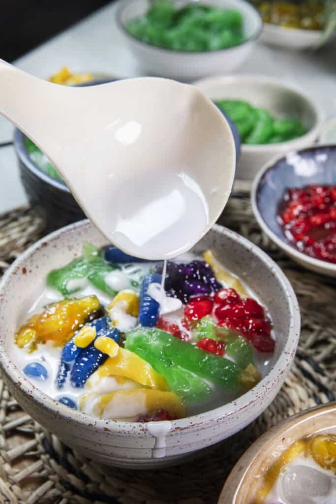 Salted coconut milk being poured over colorful Ruam Mit toppings.